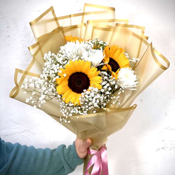 Bouquet of sunflowers and white daisies wrapped in gold paper with a pink ribbon