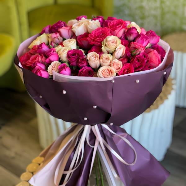 Bouquet of pink and cream roses wrapped in purple paper