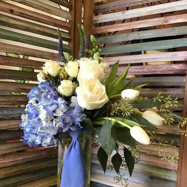 Bouquet of white roses and blue hydrangeas in a glass vase with a blue ribbon