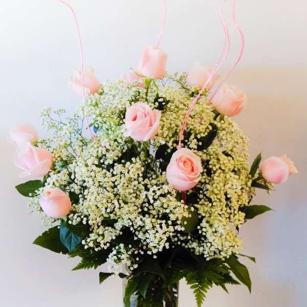 Pink roses in a glass vase with baby's breath and pink curly picks