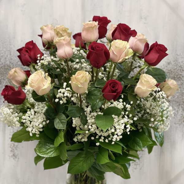 Tall arrangement of red and pale pink roses with white baby's breath in a clear glass vase