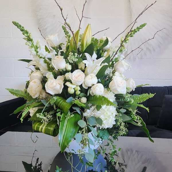 Large white flower arrangement with roses, lilies, and snapdragons in a white vase with lush greenery.