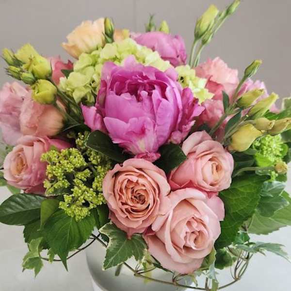 Low round arrangement of pink peonies and roses with green hydrangea in a white bowl vase