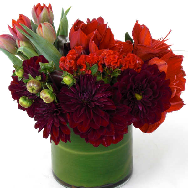 Red and burgundy flowers arranged in a green glass vase