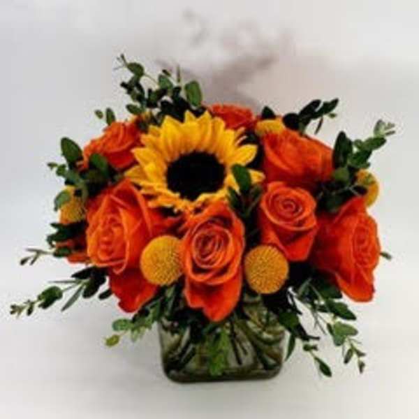 Orange roses and a sunflower arranged in a glass vase
