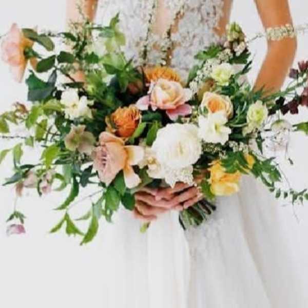 Bride holding a loose bouquet of peach, white, and yellow flowers