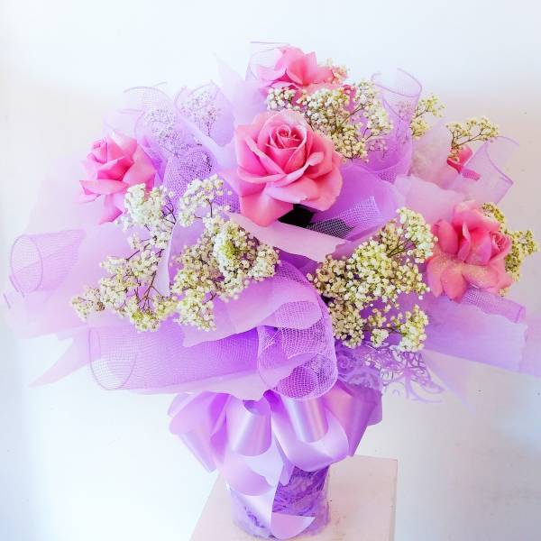 Pink roses with white baby's breath in a purple-wrapped bouquet