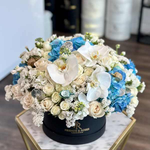 Round box arrangement of white roses, blue hydrangeas, and white orchids
