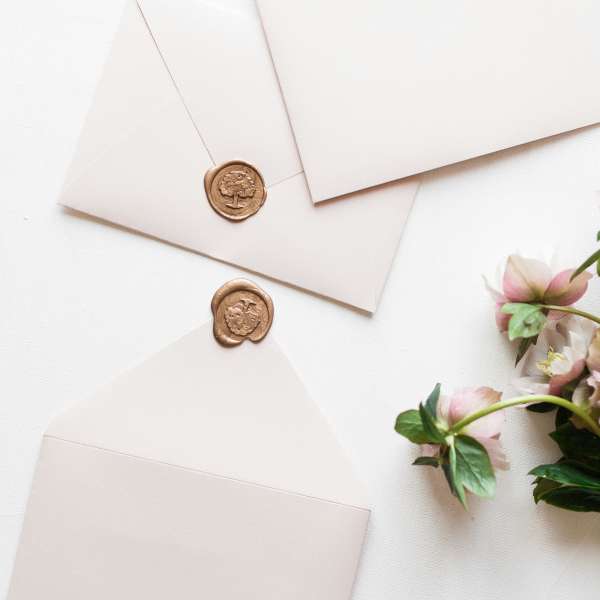 Three cream envelopes with wax seals beside pink flowers