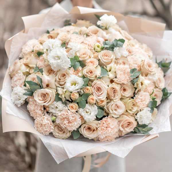Large bouquet of blush roses, carnations, and white blooms wrapped in paper