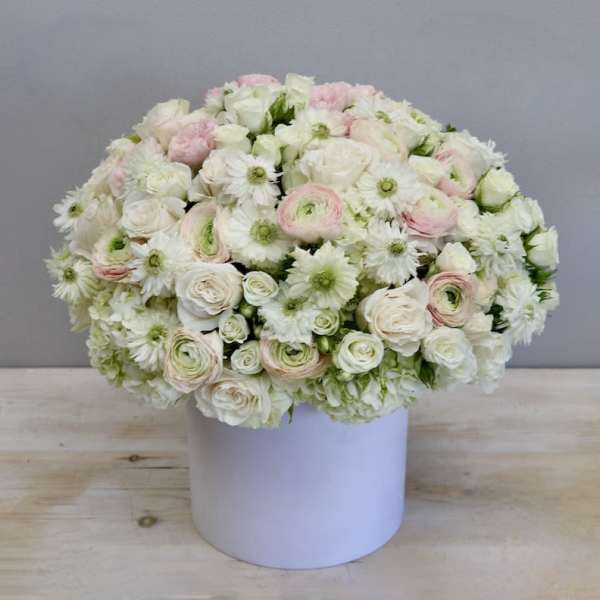 Low round arrangement of white and pale pink flowers in a white cylinder box
