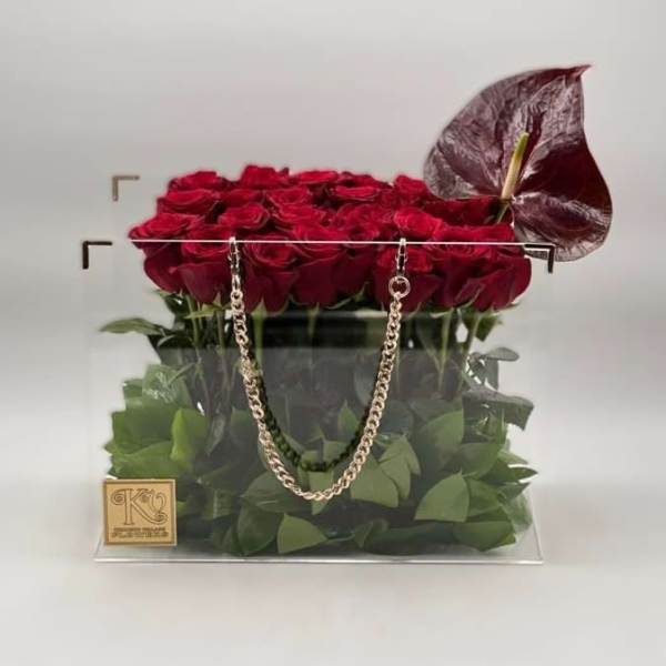 Red roses arranged in a clear square box with a decorative chain handle