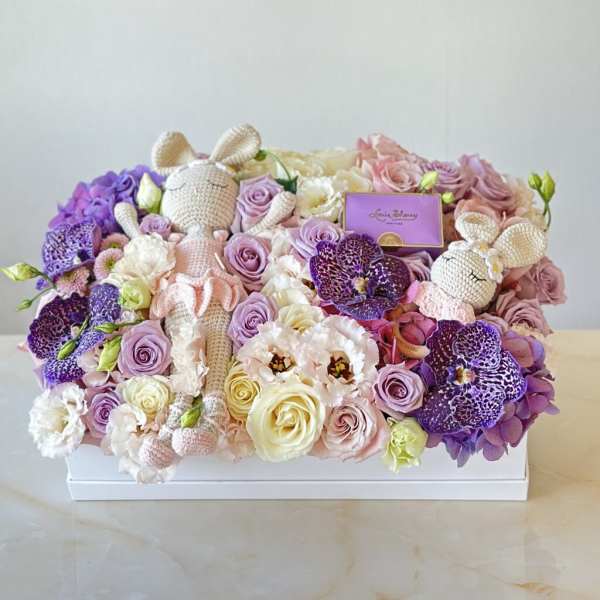 Pastel flower box with roses, orchids, and two crocheted bunny dolls