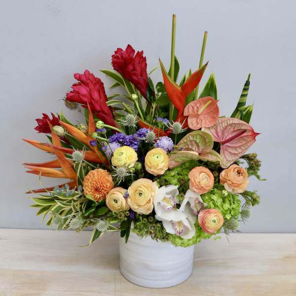 Colorful tropical flower arrangement in a white ceramic cylinder vase