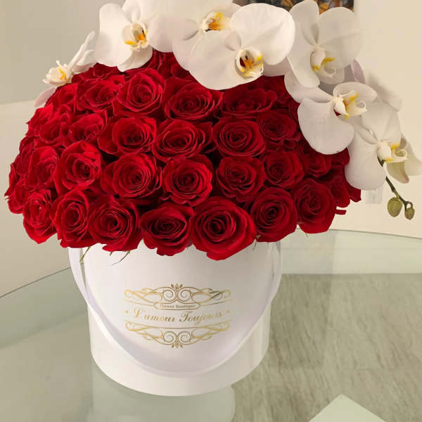 Round white hatbox packed with red roses and topped with white orchids on a glass table
