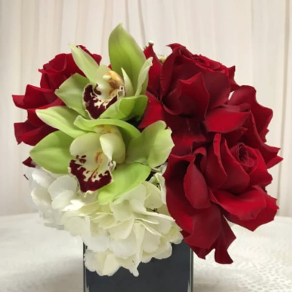 Red roses, green orchids, and white hydrangeas in a square glass vase