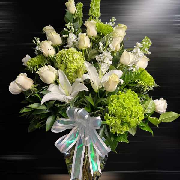 Tall vase arrangement of white roses and lilies with green hydrangeas and mums, finished with a white bow.