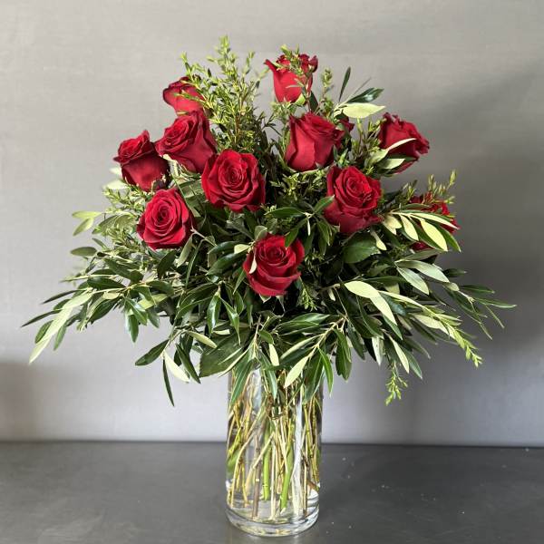 Red roses arranged in a clear glass vase with mixed greenery