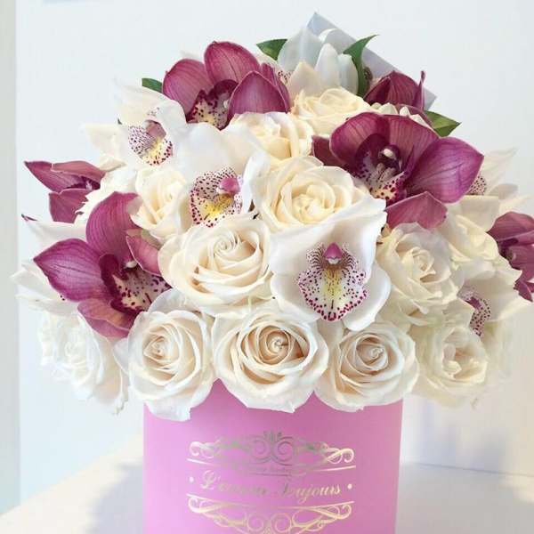 Round hatbox arrangement of cream roses and pink-purple orchids in a pink container