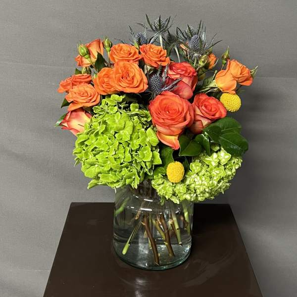 Orange roses and green hydrangeas arranged in a glass vase