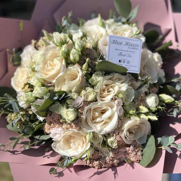 Bouquet of cream roses and small white blooms wrapped in pink paper