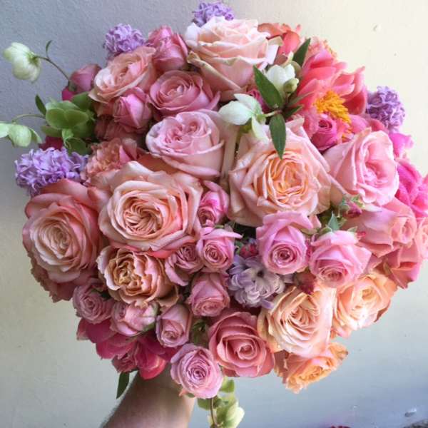 Handheld bouquet of pink and peach roses with purple accents