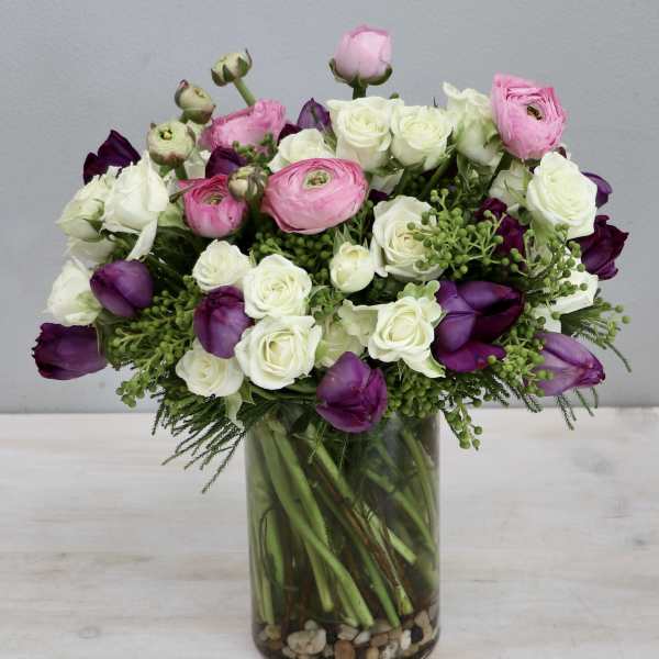 White roses with pink ranunculus and purple blooms in a clear glass vase