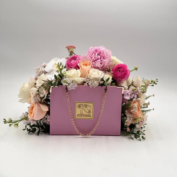 Pink and white flower arrangement in a lavender gift box with a chain handle