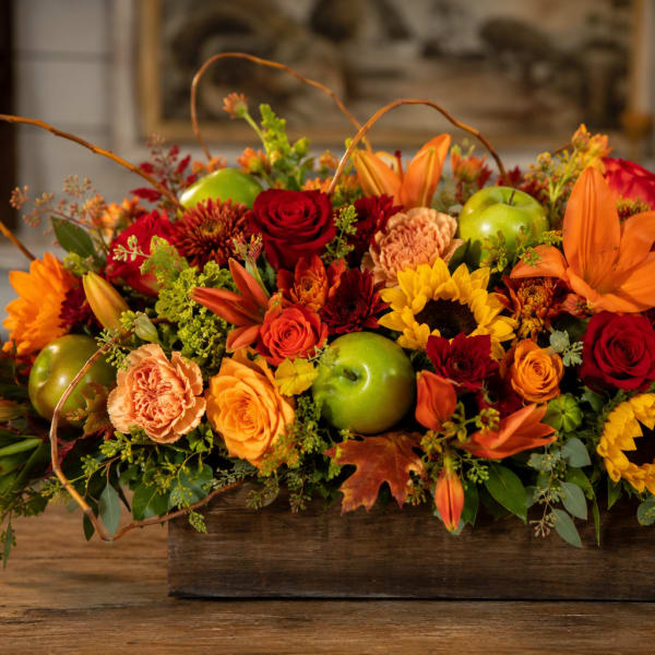 Autumn floral centerpiece with sunflowers, roses, lilies, and green apples in a wooden box