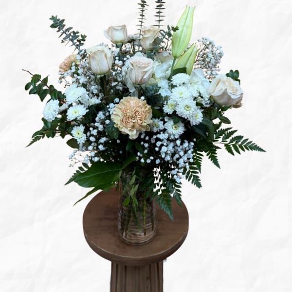 White roses and lilies arranged in a glass vase with small white filler flowers.