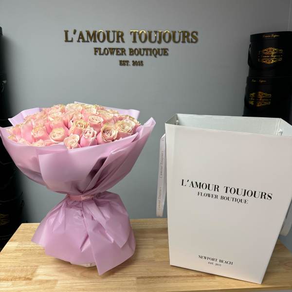 Pink rose bouquet wrapped in pale pink paper next to a tall white gift box.