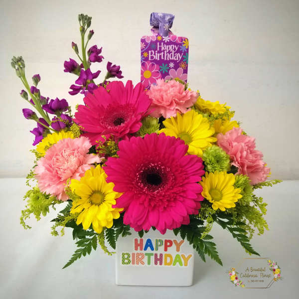 Bright mixed flower arrangement in a white birthday container