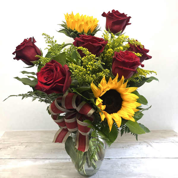 Bouquet of red roses and sunflowers in a glass vase with a ribbon