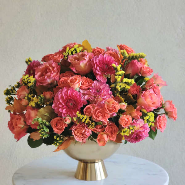 Pink and coral flower arrangement in a gold pedestal vase