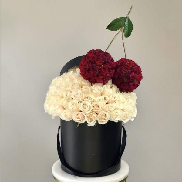 Cream and red roses arranged in a black hatbox with ribbon handles
