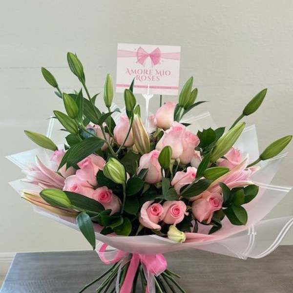 Pink roses and lily buds in a wrapped bouquet with a pink ribbon