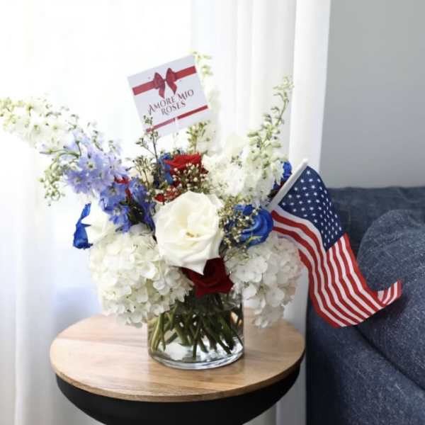 Bouquet of red, white, and blue flowers in a glass vase with small flags
