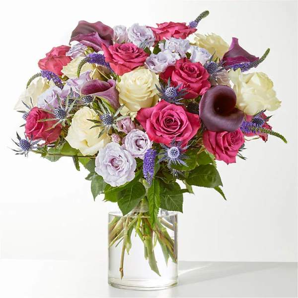Mixed bouquet of roses, calla lilies, and purple thistles in a glass vase