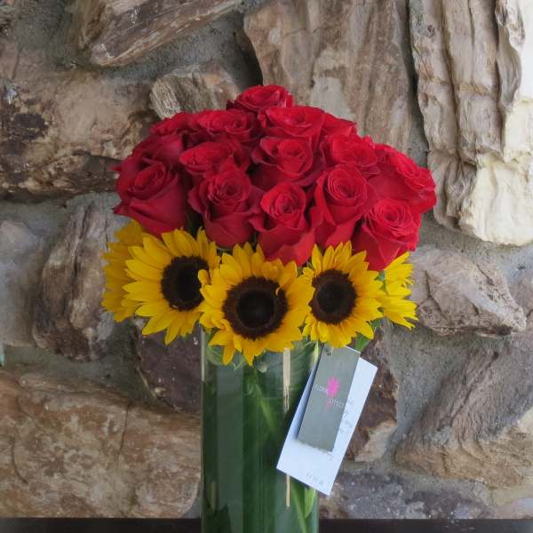 Red roses and yellow sunflowers in a tall glass vase