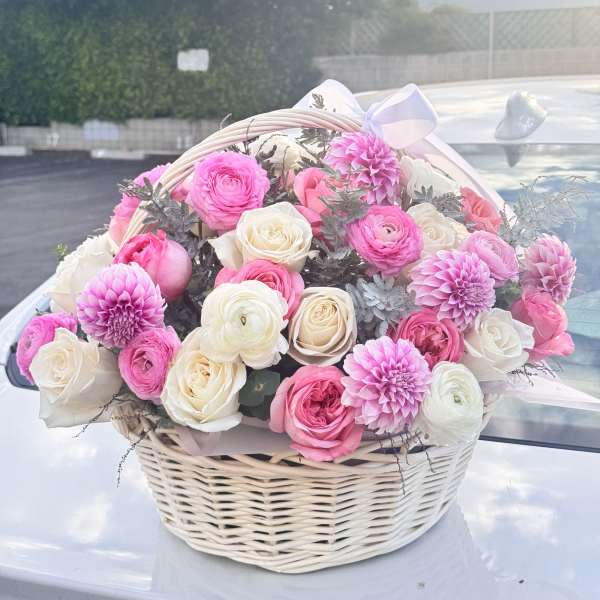 Pink and white flowers arranged in a wicker basket with a ribbon bow