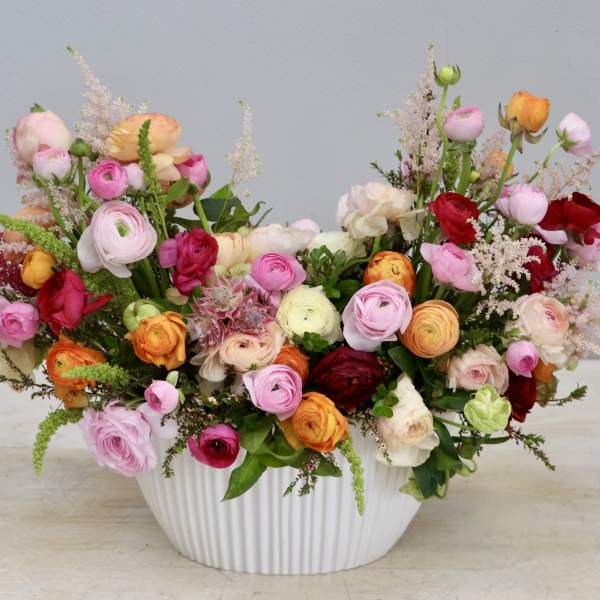 Low white ceramic bowl filled with pink, red, orange, and cream ranunculus arrangement