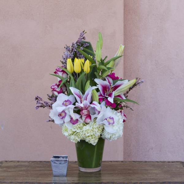 Tall bouquet of lilies, tulips, orchids, and hydrangeas in a green vase