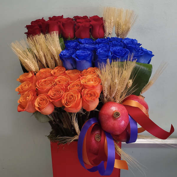 Bouquet of red, blue, and orange roses with wheat and pomegranates in a red container