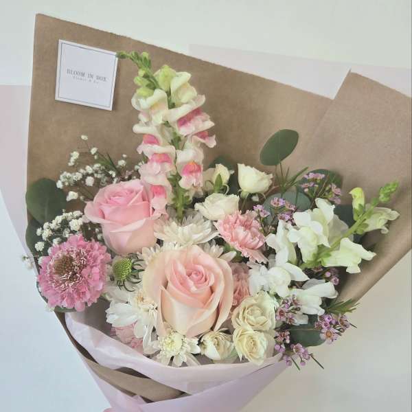 Hand-tied bouquet of pink and white flowers wrapped in brown paper