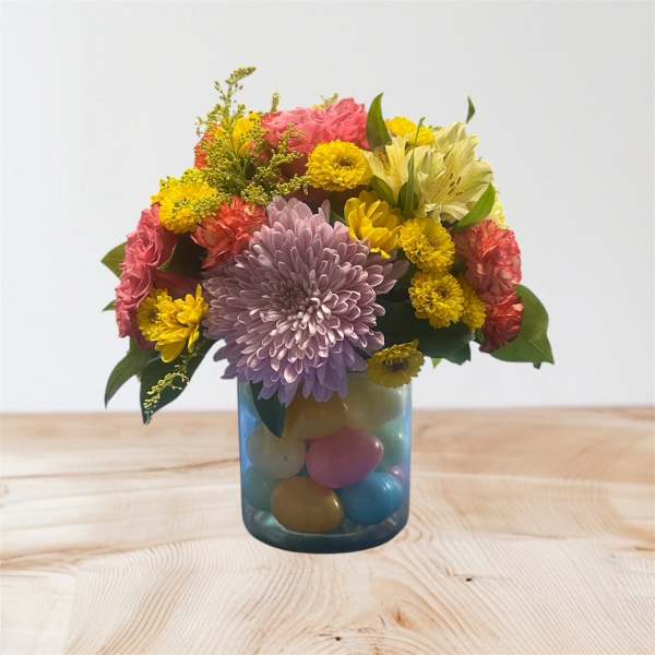 Colorful mixed flower arrangement in a blue glass vase filled with pastel eggs