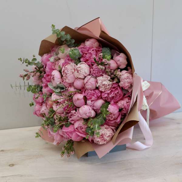 Large bouquet of pink peonies wrapped in pink and kraft paper with ribbon accents