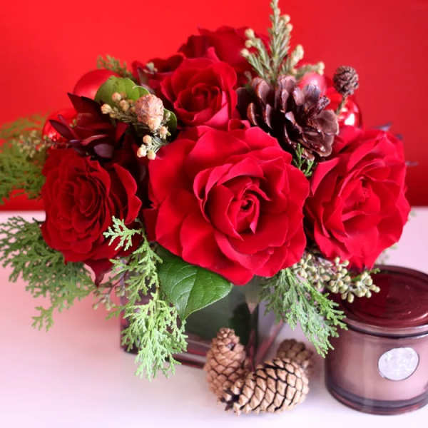 Red rose arrangement with pinecones in a glass vase
