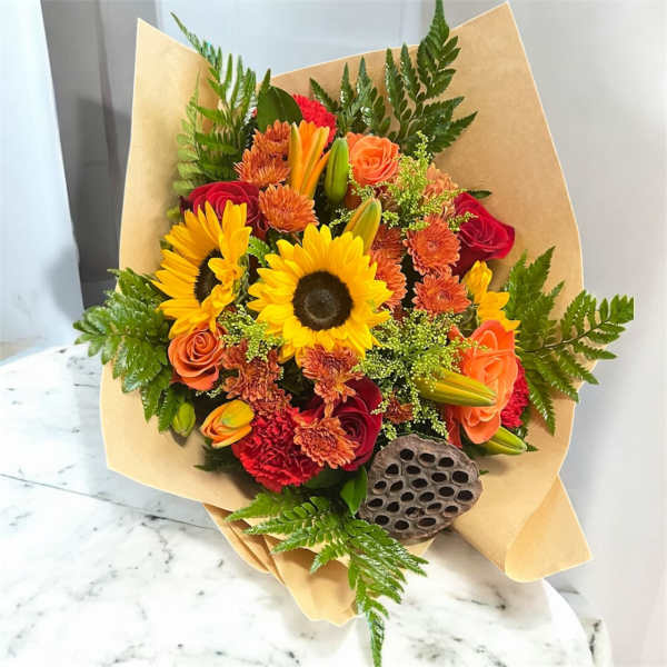 Bouquet of sunflowers, roses, and orange blooms wrapped in kraft paper
