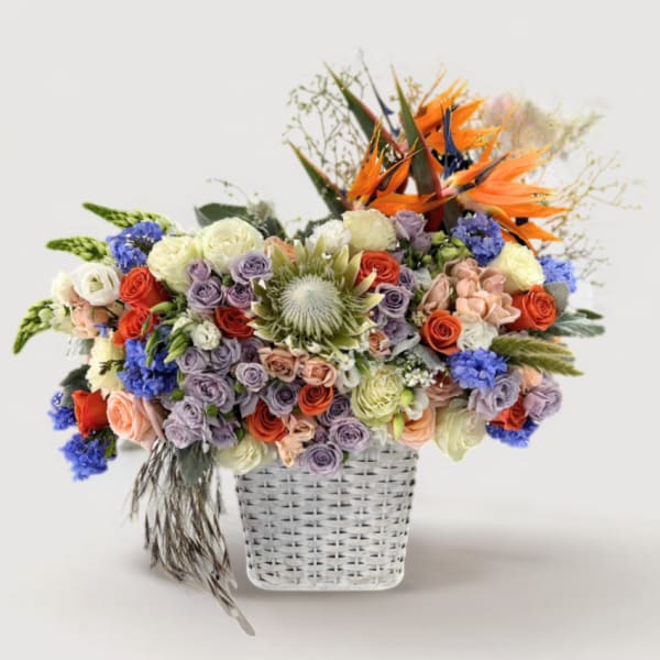 Mixed bouquet in a white woven basket with orange bird-of-paradise and pastel roses