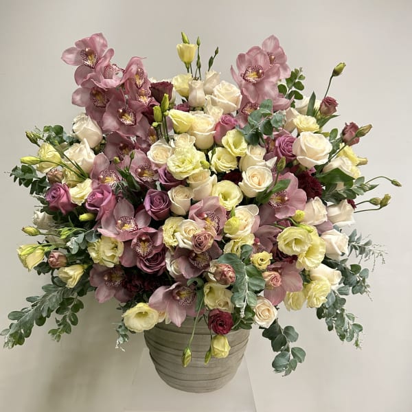 Large arrangement of cream and mauve roses with pink orchids in a gray ceramic pot